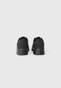 Une paire de baskets noires Replay vue de l'arrière, avec des semelles épaisses et un design minimal sur un fond clair.