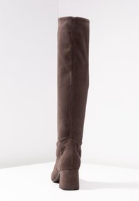 Botte marron en daim montant au-dessus du genou avec un talon épais, présentant une texture lisse et des coutures simples sur le côté.