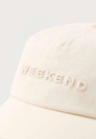 Casquette de baseball en tissu blanc cassé avec une broderie en relief formant le mot "WEEKEND" sur le panneau avant.