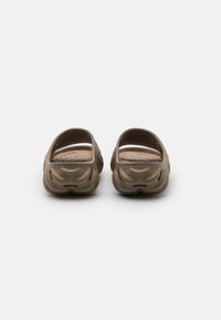 Brown slip-on shoes with a wavy textured design, open back, and flat soles, made of flexible material. Simple and functional shape.