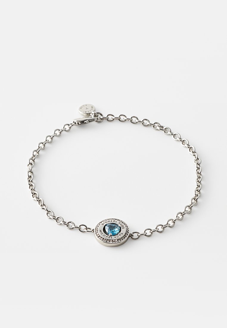 Srebrna bransoletka łańcuszkowa z centralnym owalnym niebieskim kamieniem otoczonym teksturowanym logo w obrębie. Zawiera zapięcie z regulowanym łańcuszkiem.