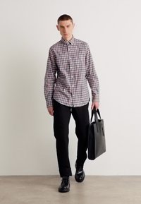 Camicia a quadri nei colori grigio, bianco e bordeaux; abbinata a pantaloni e scarpe neri; porta una borsa a tracolla nera opaca.