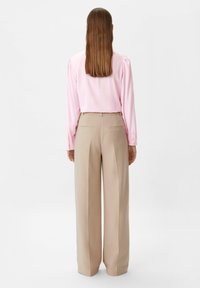 Blouse rose à manches longues associée à un pantalon beige taille haute à jambes larges. Le pantalon comporte deux poches arrière et une coupe ajustée.