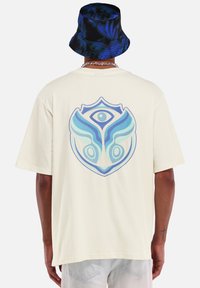 Crème oversized t-shirt met een blauw abstract grafisch ontwerp op de achterkant. Zacht katoenen stof, ontspannen pasvorm, korte mouwen, rechte zoom.