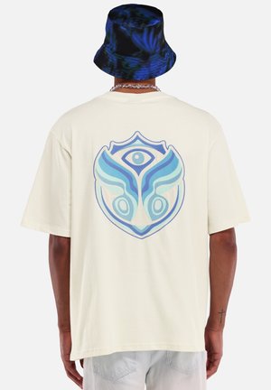 Crème oversized t-shirt met een blauw abstract grafisch ontwerp op de achterkant. Zacht katoenen stof, ontspannen pasvorm, korte mouwen, rechte zoom.