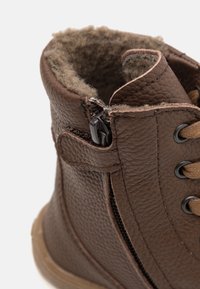 Bruine leren laars met een getextureerde afwerking, rits aan de zijkant en wollen voering aan de bovenkant. Versterkte veterogen met contrasterende veters.