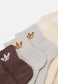 Κάλτσες βαμβακερές σε καφέ, γκρι και κίτρινους τόνους με ραμμένα λογότυπα φύλλων σε αντίθεση χρωμάτων. Κάθε ζευγάρι παρουσιάζει μια λεία υφή.