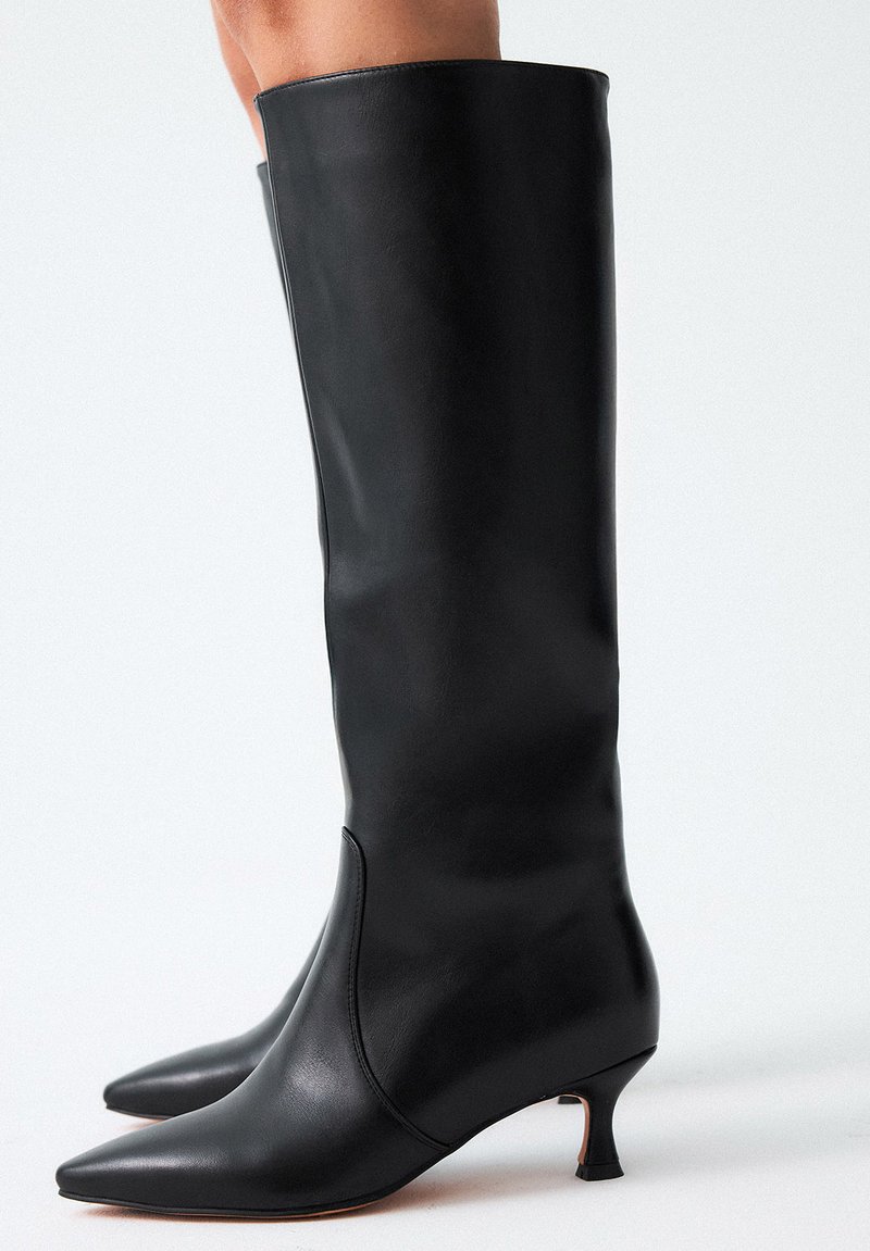 Botas de cuero negras hasta la rodilla con punta afilada y un tacón pequeño y con forma cónica. Textura lisa y diseño elegante, con acentos mínimos.