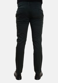 Pantaloni slim-fit verde scuro realizzati in tessuto liscio. Presentano due tasche posteriori e un design della vita standard. Indossati con scarpe nere.