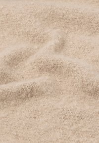 Beige krāsas tekstūrēta auduma ar mīkstu, pūkainu virsmu. Materiāls izskatās viegls, ar nedaudz nevienmērīgu, cilpu rakstu.