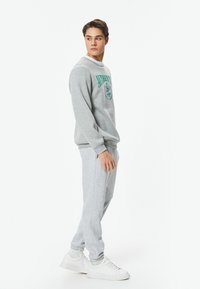 Grå sweatshirt med grøn grafisk tekst og logo, parret med matchende grå sweatpants og hvide sneakers. Blødt materiale, afslappet pasform.