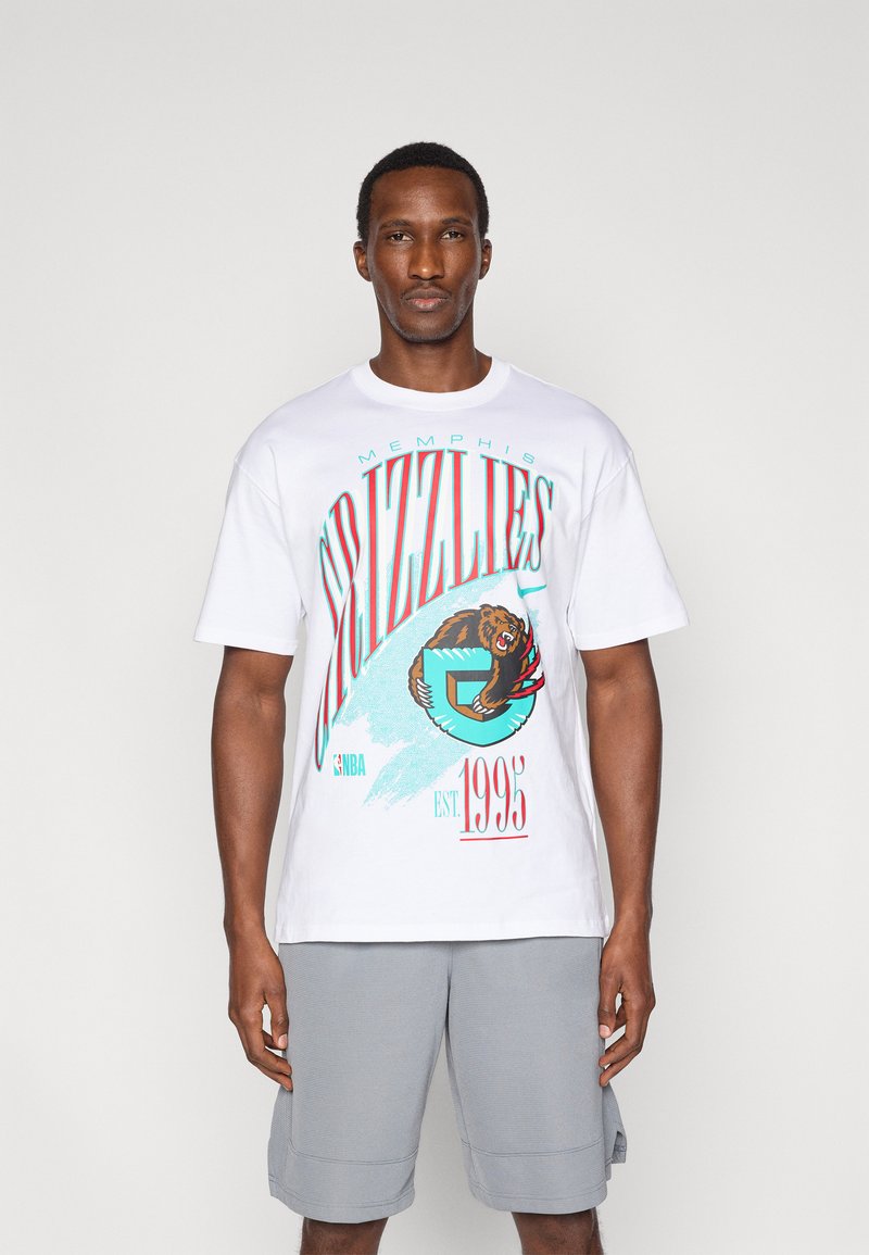 Λευκό βαμβακερό μπλουζάκι με γραφικά των Memphis Grizzlies σε τιρκουάζ και κόκκινο, κοντά μανίκια και λαιμόκοψη. Φορεμένο με γκρι σορτς.