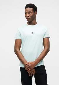 Μέντα πράσινο βαμβακερό μπλουζάκι με κεντρικό λογότυπο σε κόκκινα, λευκά και μπλε στοιχεία. Κοντά μανίκια, στρογγυλή λαιμόκοψη. Συνδυάστε με σκουρόχρωμο παντελόνι.