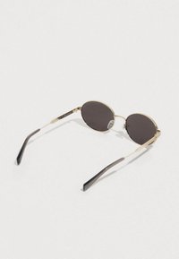 Kerek napszemüveg sötét lencsékkel, arany fém kerettel és fekete műanyag szárakkal. A kereten részletgazdag díszítések találhatók.