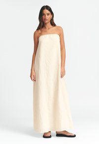 Trägerloses cremefarbenes Maxikleid aus strukturiertem Stoff mit geradem Ausschnitt. Kombiniert mit schwarzen flachen Sandalen, zeigt es eine fließende Silhouette.