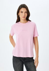 Camiseta de algodón rosa con mangas cortas, que presenta la palabra "Creativo" bordada en un tono ligeramente más oscuro en la parte delantera.