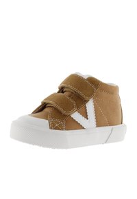 Zapato alto de ante marrón con dos correas de Velcro, suela de goma blanca y detalle en diseño en V blanco contrastante en el lateral.