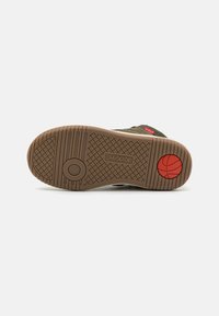 Suela de zapato con un diseño de goma marrón texturizada, que presenta un acento rojo circular y un logo. El patrón incluye estrías y círculos para mejorar el agarre.
