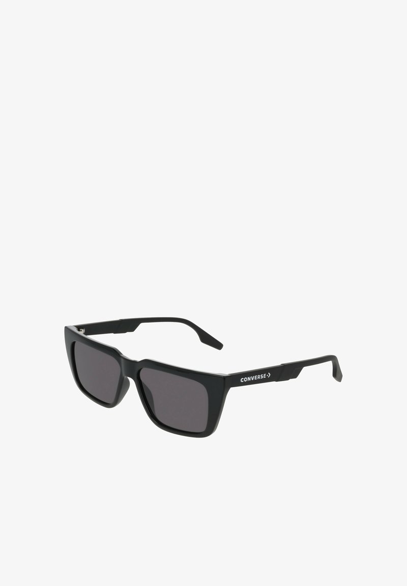 Czarne prostokątne okulary przeciwsłoneczne z ciemnymi szkłami, matową plastikową oprawką i białym logo „CONVERSE” na boku, wyposażone w proste zauszniki.