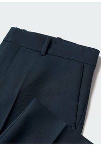 Pantalon bleu marine ajusté avec passants de ceinture et pli sur le devant, plié sur un fond clair.