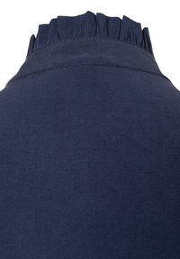 Chemise bleu marine avec un col froncé et un tissu lisse et texturé. Le col présente un volant décoratif le long du bord.