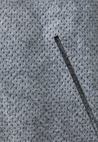Grå perforert stoff med en teksturert overflate, med små hull og et smalt snitt i materialet for designdetaljer.