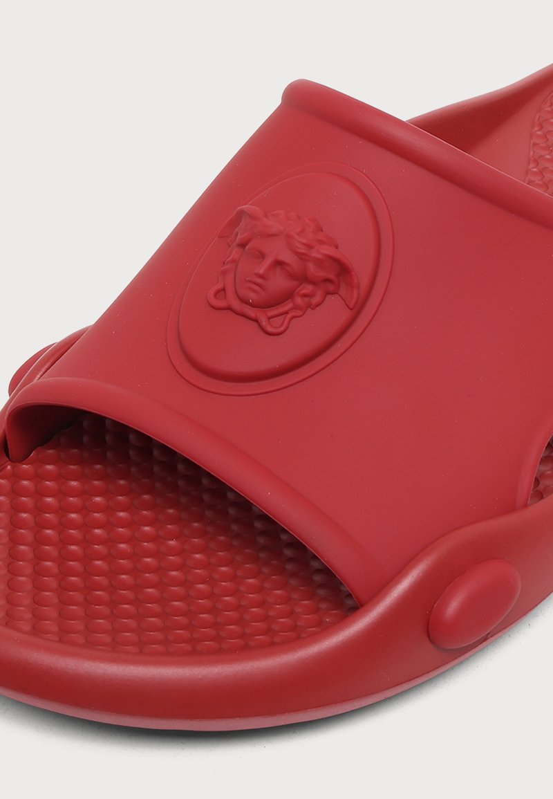 Roter Slip-On-Sandal mit strukturiertem Fußbett und erhabenem Medusa-Kopf-Logo auf dem Riemen.