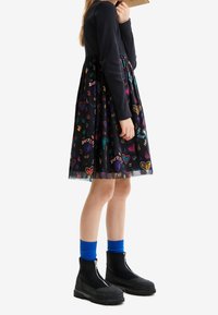 Sukienka z prążkowanym granatowym topem i czarną spódnicą zdobioną kolorowymi wzorami serc i tekstu. Do tego czarne buty na zamek i niebieskie skarpetki.