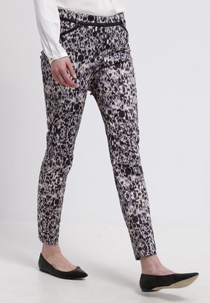 Slim-fit enkellange broek met zwart-witte abstracte dierenprint, gedragen met zwarte ballerina's en een wit overhemd met lange mouwen.