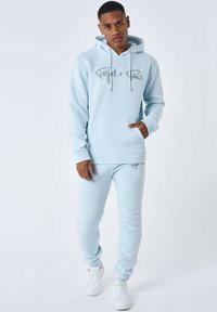 Felpa azzurra chiara con tasca a marsupio e logo, abbinata a pantaloni jogger coordinati in azzurro chiaro. Realizzata in tessuto morbido, con caviglie elasticizzate.
