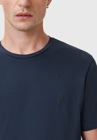 Mörkblå bomullst-shirt med rund hals och korta ärmar. Har en diskret svart broderad logotyp på bröstet. Mjuk textur.