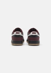 Baskets Nike avec un dessus bordeaux et noir, des accents argentés et un dos texturé, présentant une semelle en caoutchouc avec un motif en chevron.