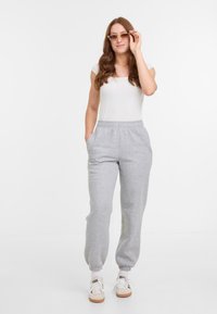 Pantalons de survêtement gris clair avec des poignets élastiques, des poches latérales et une taille avec cordon, associés à un débardeur blanc ajusté et des baskets.