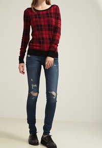 Rutig långärmad tröja i röd och svart med rund halsringning, tillsammans med slitna blå skinny jeans och svarta snörskor med nitar.