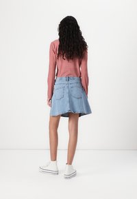 Jeansrock, hellblau, ausgestellte Form mit Gesäßtaschen, kombiniert mit einem rot-weiß karierter Langarmbluse und weißen High-Top Sneakers.