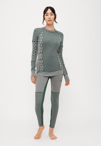Conjunto de ropa activa en verde y gris con estampados, que incluye una camiseta de manga larga y leggings, con diseños geométricos, rayas y texturas variadas.