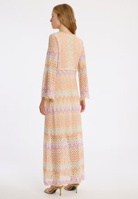 Robe maxi à manches longues, présentant un motif en zigzag dans des couleurs pastel. Conçue avec un corsage ajusté et une jupe fluide, fabriquée en tissu texturé.