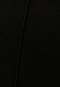 Noir, vue en gros plan d'un tissu texturé avec une finition lisse, présentant une couture verticale au centre.