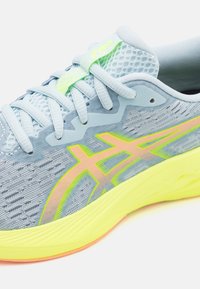 Scarpa sportiva di colore azzurro chiaro con tomaia in rete, presenta dettagli in neon giallo e rosa, punta arrotondata, suola testurizzata e dettagli riflettenti.