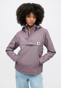 Lila vindjacka med halvlång dragkedja, justerbar huva och logotypmärke på bröstet. Har sidofickor och elastiska ärmslut.