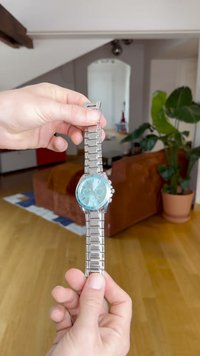 Silver metal bracelet watch with a light blue face, features chronograph sub-dials, stainless steel links, and a polished finish.
