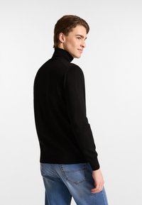 Schwarzer Rollkragenpullover aus weichem Strickmaterial. Hat lange Ärmel, eine taillierte Passform und eine glatte Textur. Kombiniert mit hellblauen Jeans.