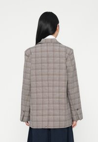 Geruite blazer in grijs, bruin en taupe tinten, gestructureerde pasvorm, twee knopen op de mouwen en gegoten revers. Eenvoudige achterkant zonder zichtbare details.