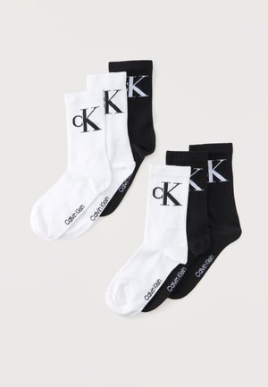 Kaks komplekti kolme Calvin Kleini crew-sokki mustas ja valges, igaühel "cK" logo pahkluu peal ja brändi nimi jalal.