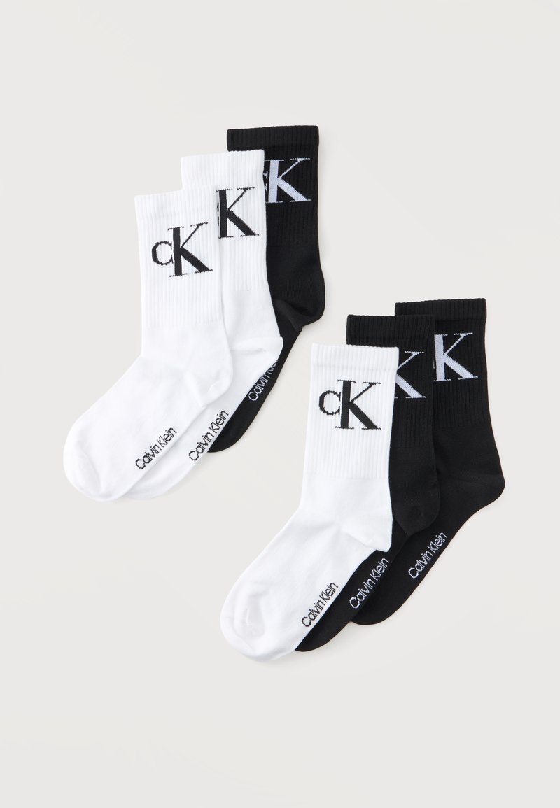 Δύο σετ από τρία καλσόν Calvin Klein σε μαύρο και λευκό, το καθένα με το λογότυπο "cK" στον αστράγαλο και το όνομα της μάρκας στο πέλμα.