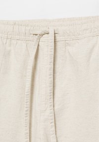Pantalon en tissu beige avec une taille élastique et un cordon noué au centre devant.