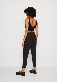Must muströöp tõmblukk ja sügava selja lõikega must cropped top, kombineeritud kitsaste mustade pükste ja massiivsete mustade kingadega. Sile tekstuur ja minimalistlik disain.