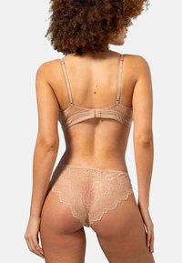 Nud spetsbh och matchande trosor. Bh:n har justerbara band och haktillclosing; trosorna har scalloperad spetsdetalj och mjuk textur.