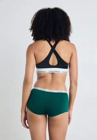 Black sports bra with cross-back design and white Calvin Klein logo. Green hipster shorts with elastic waistband, also featuring logo.