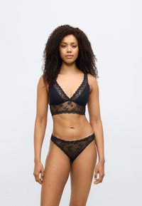 Černá krajková podprsenka typu bralette a ladící tanga s vroubkovanými okraji, zdobené průsvitným květinovým vzorem a trojúhelníkovými košíčky, nabízející jemný design.